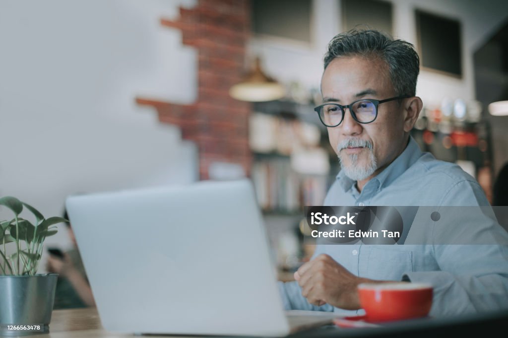 an asian chinese senior man having discussion with his colleague via online virtual meeting in a cafe an asian chinese senior man having discussion with his colleague via online virtual meeting Senior Adult Stock Photo