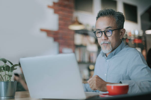 um homem chinês chinês sênior tendo discussão com seu colega via reunião virtual on-line em um café - computer coffee laptop business - fotografias e filmes do acervo