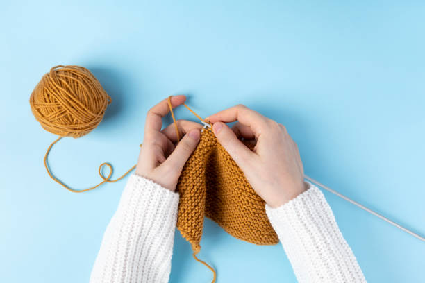 mãos femininas tricotando com lã amarela, fundo azul. vista superior - sweater cardigan knitting blue - fotografias e filmes do acervo