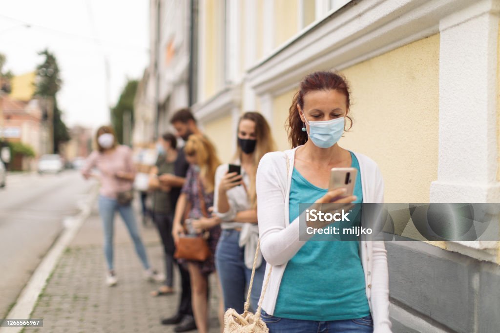 Waiting in line - Social distancing People are standing in line and waiting in front of the building entrance. There is a proper distance between them because of social distance rule during the corona virus. Everyone wearing protective face masks Waiting In Line Stock Photo