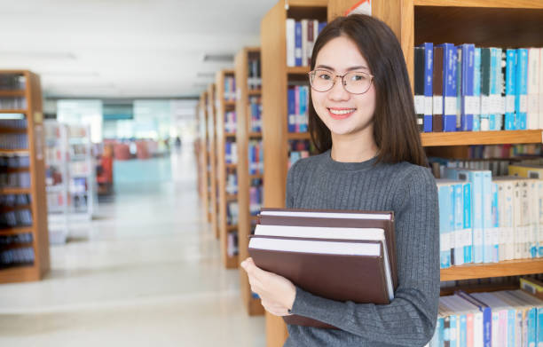 istock Back to school education knowledge college university concept, Beautiful female college student holding her books smiling happily standing in library, Learning and education concept 1266568364