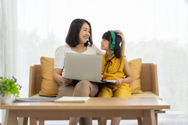 Asian young mother with computer notebook teaching kid to learn or study online at home, Homeschooling online concept stock photo