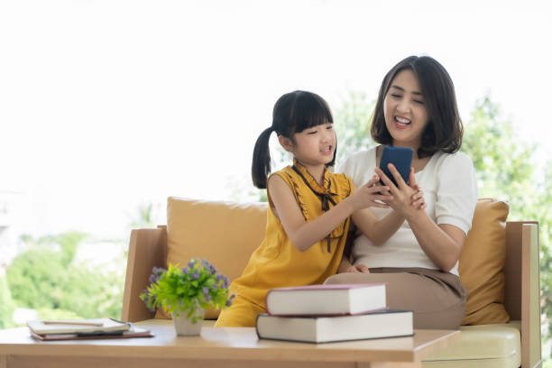Asian mother and daughter kid using smartphone at home, Homeschool learning concept stock photo