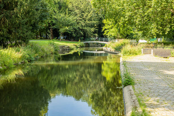 istock Stream with reflection in the water surrounded by lush trees and a small pedestrian bridge in the background in a park in the city of Maastricht 1266569489