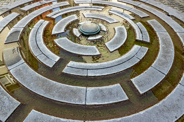 Modern circular fountain with geometric shaped grooves with water circulating and reflection of sunlight in the water stock photo