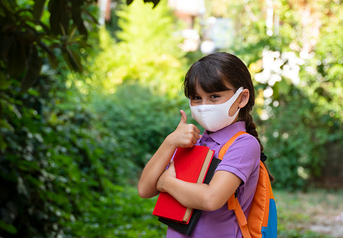 Cute little girl wearing backpack and facial mask to protect herself from coronavirus, she is ready for back to school