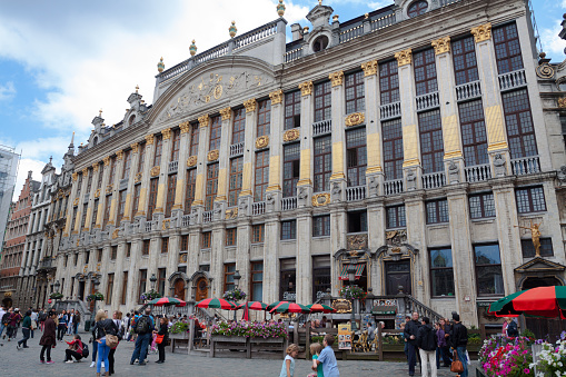 Facade of Maison Grand Place in Brussels. People and tourists are on square and are walking around. In bottom area of building are tables of a restaurant
