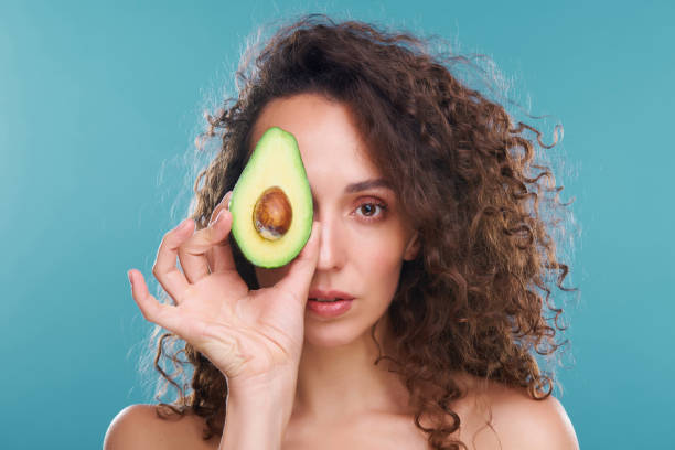 istock Young woman looking at you with left eye while holding avocado by another one 1266578139