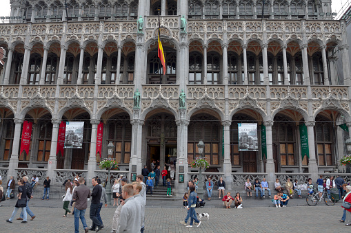 Tourists outsid eof Maison du Roi at Grand Place in Brussels. Maison du Roi is opposite to old town hall. People are crossing square or are sitting at steps of building.