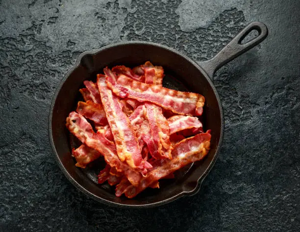 Photo of Fried crunchy Streaky Bacon pieces in a cast iron skillet