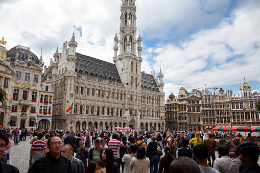 Crowd of international and asian tourists on Grand Place in Brussels in summer. View over heads of people. In background is old town hall Hotel de Ville.