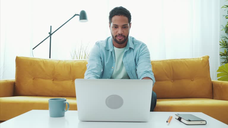 Young man working remotely from his house comfort using his laptop. He is managing his business away from office.