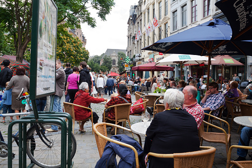 Crowd and relaxing people at restaurants in street Rue Marche aus Herbes in Brussels near Grand Place in summer. View along sidewalk and over tables of restaurants under parasols. A lot of people are in street