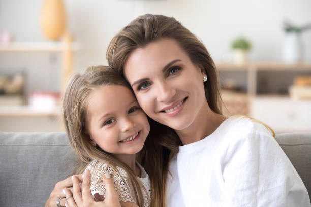 istock Beautiful mother and daughter sitting on couch looking at camera 1266588149