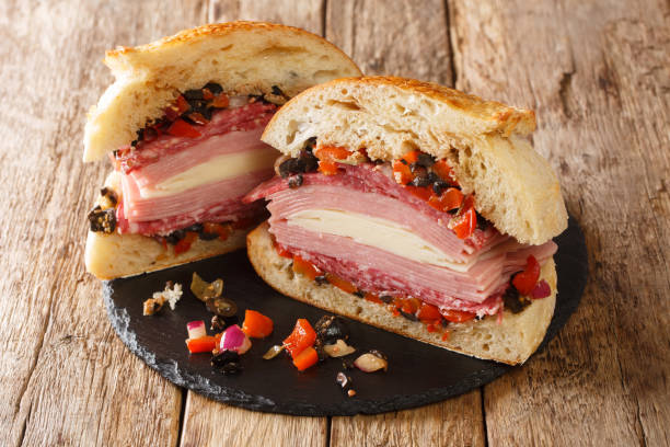 new orleans muffuletta sandwich a monster of a sandwich piled high with multiple types of meat and cheese, and a perky olive salad close up on a slate board. horizontal - restaurant pasta italian culture dinner imagens e fotografias de stock