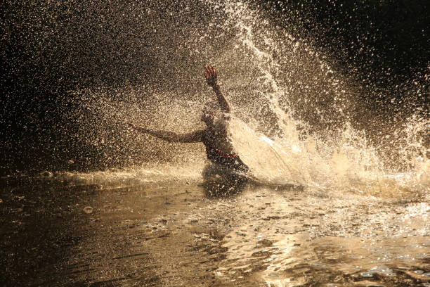 Young woman running and diving into river with water droplets backlit by sunshine
