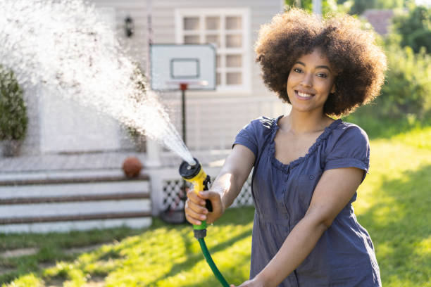 istock Young afro woman having fun when spraying with garden hose 1266594788