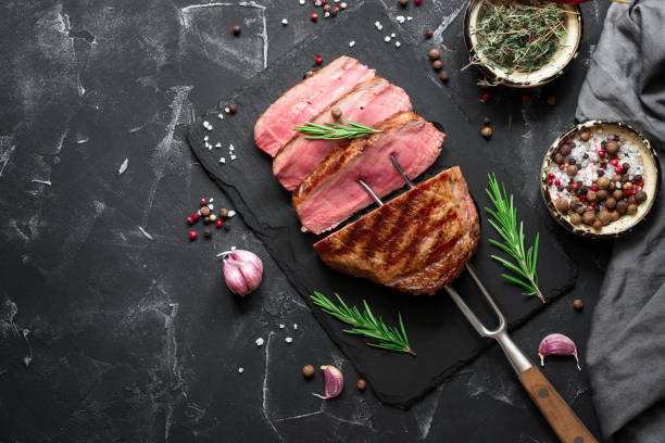 istock Grilled ribeye beef steak medium rare with spices and herbs on a black stone background. Top view, flat lay, copy space. 1266594895