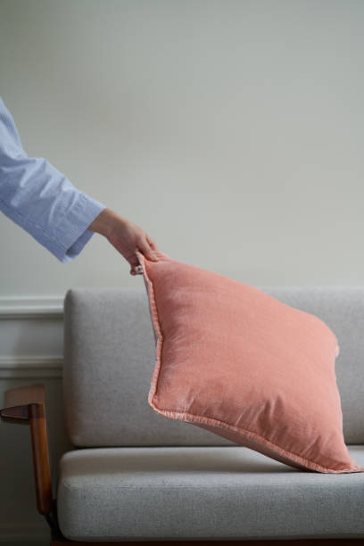 Young woman arranging pillows on sofa cushions at home. Maid service, housework and cleaning concept.