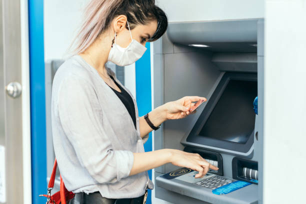 istock Young woman with protective face  mask while withdrawing money at ATM 1266597292