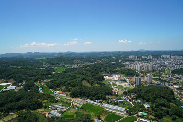 A panoramic view of contemporary residential buildings set against a backdrop of lush green hills under a clear blue sky. The scene captures the harmony between urban development and nature, offering a serene yet vibrant atmosphere ideal for real estate promotions or environmental campaigns.