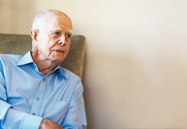istock Man in his 80s sits on a chair looking towards a blank wall for use as copy space 1266608220