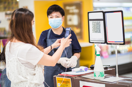 An Asia Chinese woman scanning QR code registering herself and check in using mobile app before entering the supermarket as new standard operating procedure for Covid-19. Safety precaution