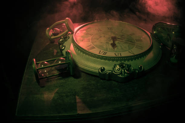 istock Time concept. Big vintage round clock on wooden table with abstract light. 1266608819