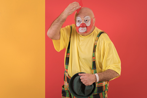 Portrait of a senior male circus clown in front of colored background