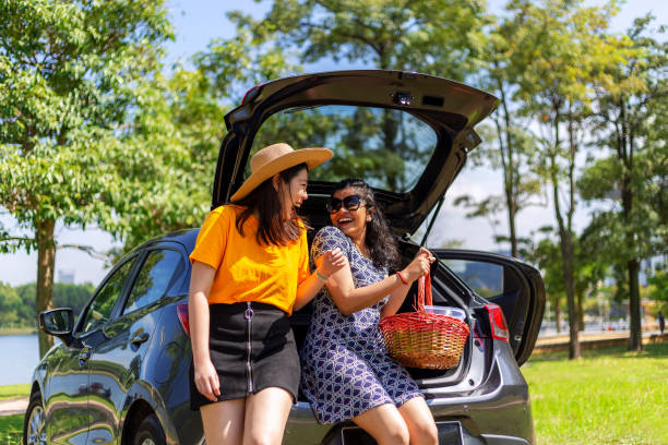 young women sitting on car trunk, chatting happily