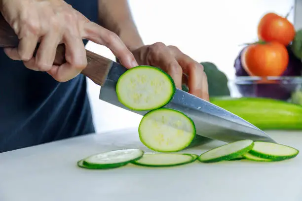 Close up hands women holding knife and cuting fresh Courgette on Cutting Board. Female hand slices raw Japanese Cucumber into circles with knife on cutting Board. healthy food concept..