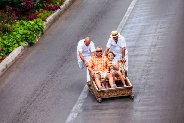 FUNCHAL, MADEIRA - JULY 04, 2014: Toboggan riders pushing sledge with tourists near Monte Palace Tropical Garden in Madeira island, Portugal