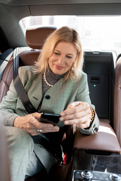 счастливый блондинка зрелые женщины обмена сообщениями в смартфоне, сидя в такси - mobile phone seat belt text messaging smiling стоковые фото и изображения