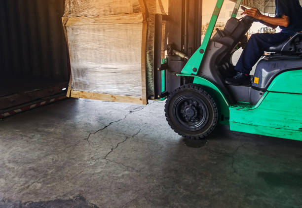 istock Worker driving forklift loading and unloading shipment carton boxes and goods on wooden pallet from container truck to warehouse cargo storage in freight logistics and transportation industrial 1266638451