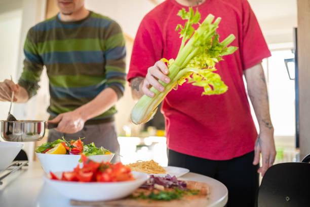 Gay couple about to have a healthy lunch Gay couple taking sauce for spaghetti and fresh celery to have lunch at the dining table gay dinner table stock pictures, royalty-free photos & images