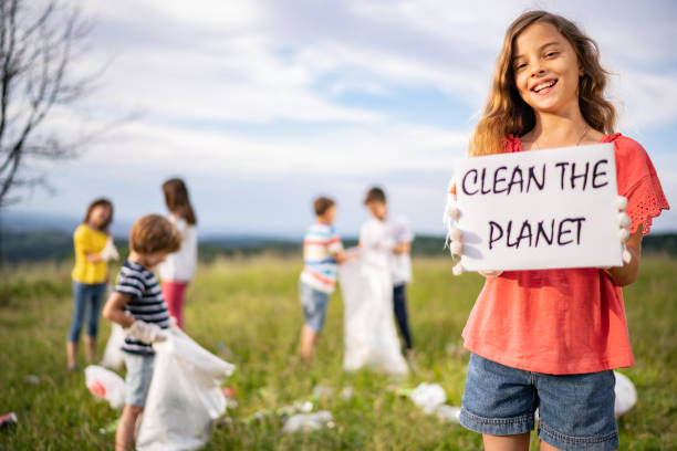 Girl with messages "Clean the Planet" Smiling girl holds a message about nature while other kids collecting garbage climate justice stock pictures, royalty-free photos & images