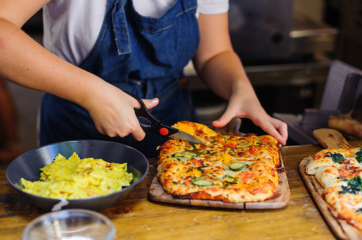 Chef hands cuts pizza with kitchen scissors