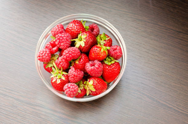 Transparent bowl with strawberries and raspberries close-up top view. Ripe, juicy berries. Summer vegetarian food.