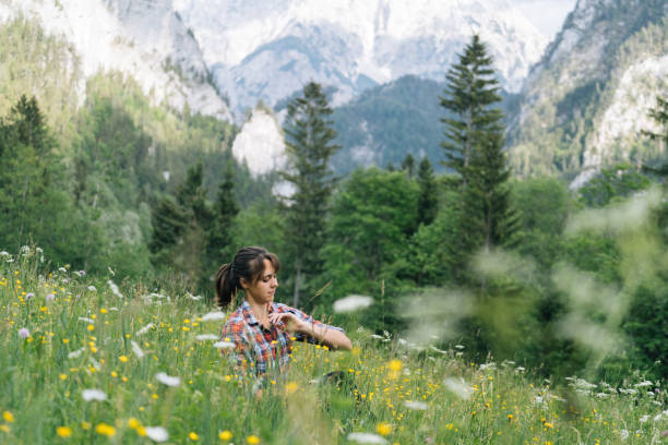 istock Young woman sits in mountain meadow and examines an insect 1266644621