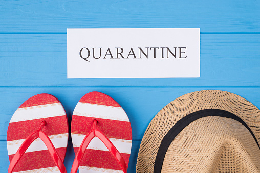 Summer vacation and quarantine concept. Top above overhead view photo of word quarantine flipflops and hat isolated on blue wooden background