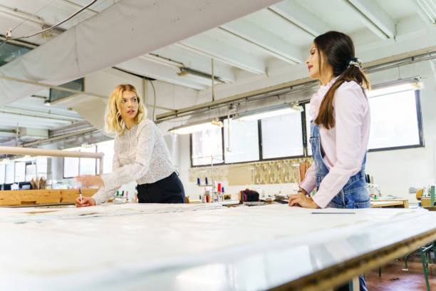 istock Two female workers at factory talking about ongoing project - Woman making sketch design while her friend is watching and giving advice or critique - Real people brainstorming development concept 1266653340