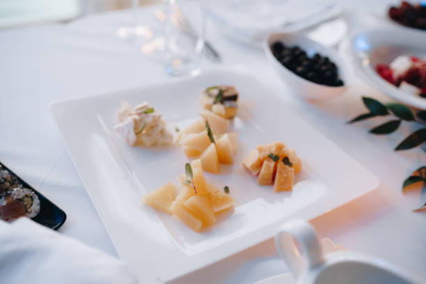 istock A square plate with different types of sliced cheese on a white tablecloth next to a bowl of black olives. 1266655742