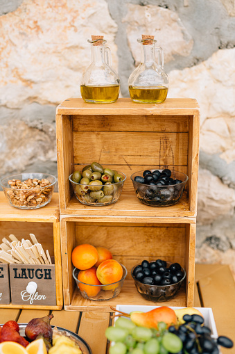 Large black and green olives in glass salad bowls and two glass jugs for olive oil on a wooden stand on a table with walnut kernels and exotic fruits. High quality photo