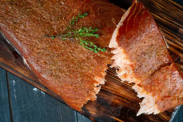 Photo of A half-torn piece of smoked salmon fillet on a wooden Board on a dark background