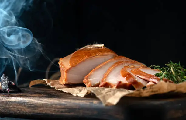 Photo of Smoked breast chicken fillet whole and sliced on wooden board. Rustic natural food