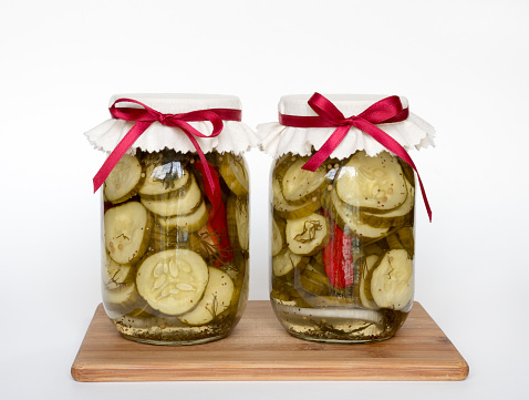 Home canned dill pickles in pint  jars with cream cap tied with red ribbon isolated on white background.