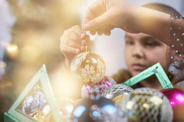 Family preparing to celebrate Xmas. Son helps mom to decorate the Christmas tree. Taking Christmas ornate from a box and putting on the tree