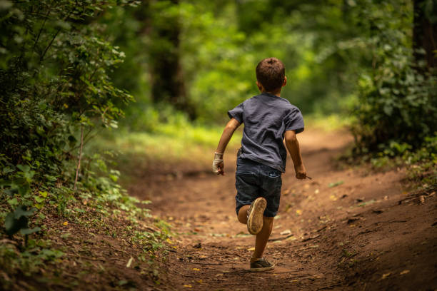 Liitle boy running on dirt road in forest among trees