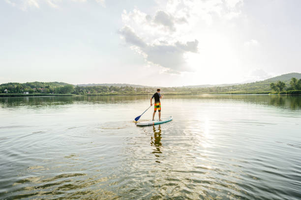 One woman paddleboarding at the lake at sunset