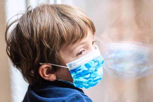 istock Sad pensive little boy wearing a protective face mask looking out through his school window 1266669729